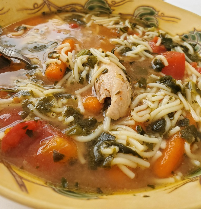 A bowl of chicken soup with spinach, carrots, and cut up spaghetti