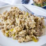 A serving of hamburger rice casserole next to a fork on a white plate.
