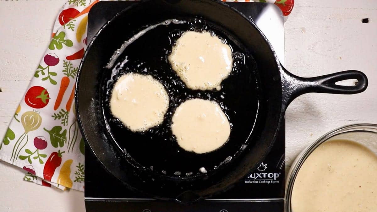 Close-up of golden brown hoe cakes cooking in a cast iron skillet