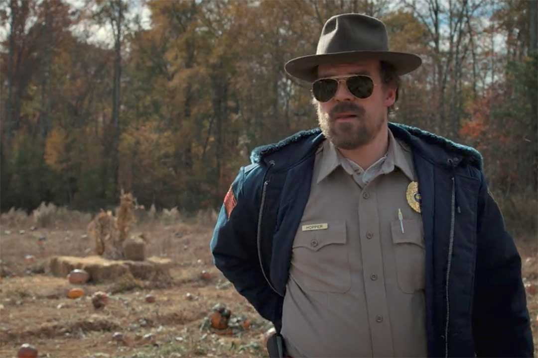 Hopper from Netflix series Stranger Things wearing police uniform and wire Aviator sunglasses outside on sunny day