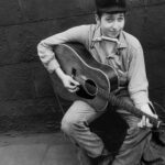 Bob Dylan in his early years, wearing a simple button-down shirt and a cap, embodying the folk singer style