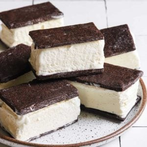 A close-up of homemade ice cream sandwiches on a white plate with a brown rim, highlighting the rich chocolate color and creamy ice cream filling.