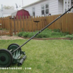 Man using an old fashion lawn mower in a backyard, cutting the grass neatly.