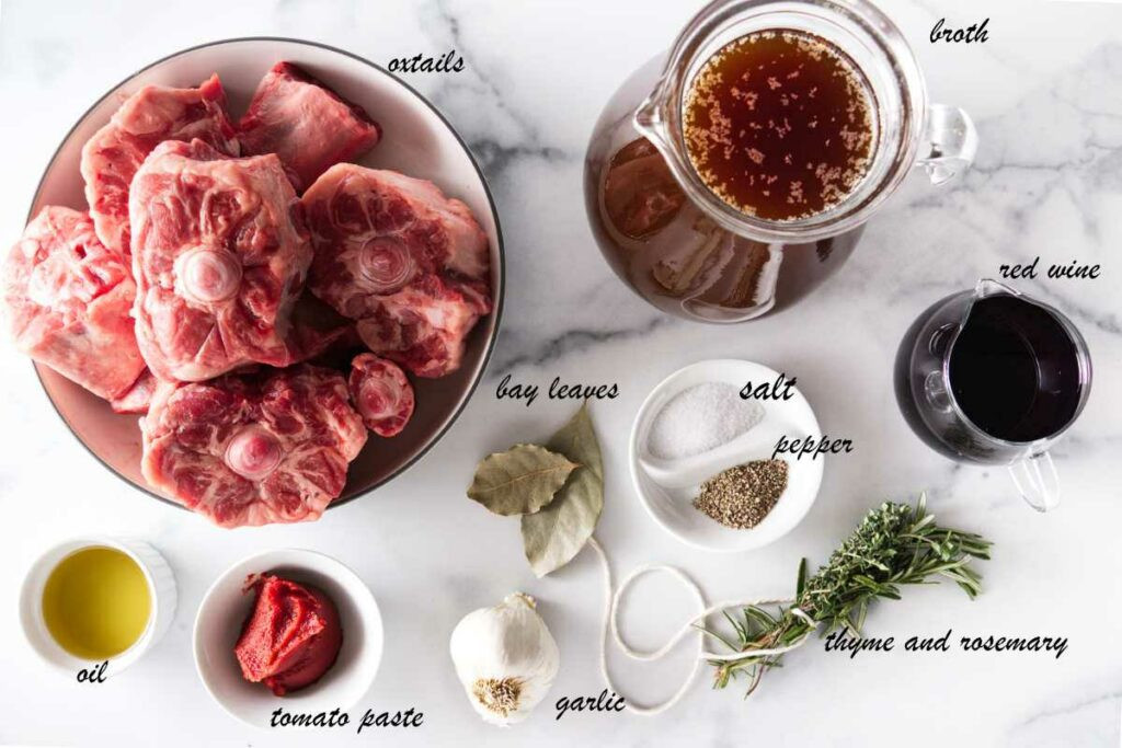 Ingredients for oxtail soup, including oxtails, beef broth, wine, fresh herbs, salt, pepper, garlic, tomato paste, and oil.
