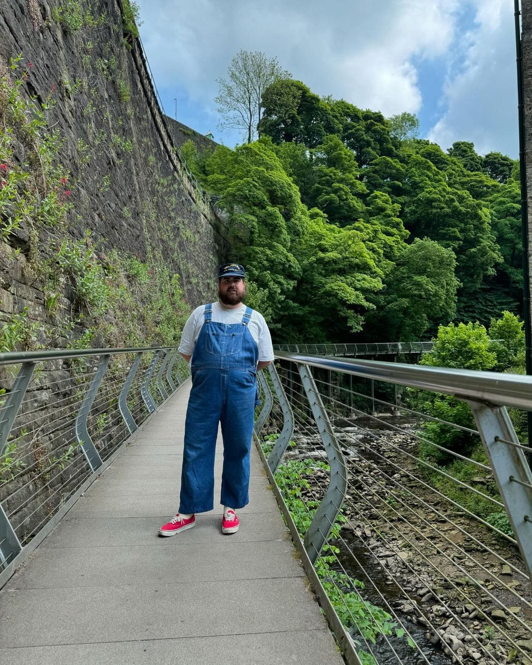 man wearing blue denim overalls with a white t-shirt and white sneakers