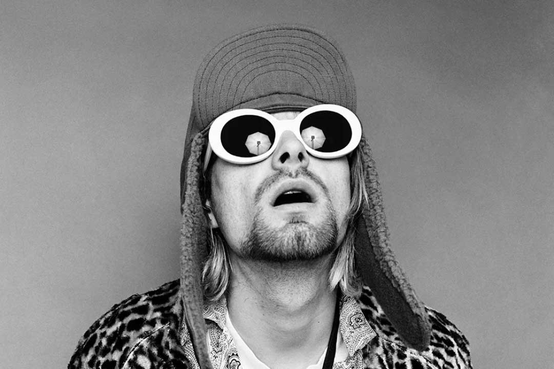 Kurt Cobain wearing round white sunglasses looking upwards with his mouth open