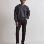 man wearing black jeans, a grey crewneck sweatshirt, and black lace-up shoes, showing a casual yet sophisticated style