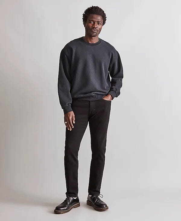 man wearing black jeans, a grey crewneck sweatshirt, and black lace-up shoes, showing a casual yet sophisticated style