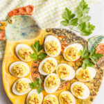 Deviled eggs served on a rooster egg plate with sprigs of parsley for garnish.
