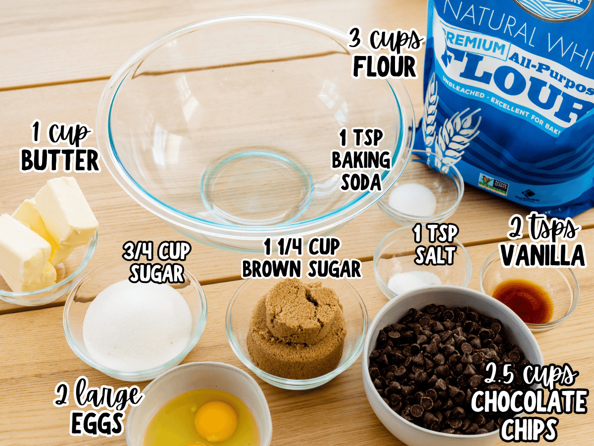 A collection of essential cookie ingredients arranged on a wooden countertop, highlighting butter, eggs, vanilla extract, flour, and chocolate chips.
