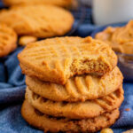 Old-fashioned peanut butter cookies with fork prong lattice on top. One cookie has a bite taken out of it to show crisp texture.