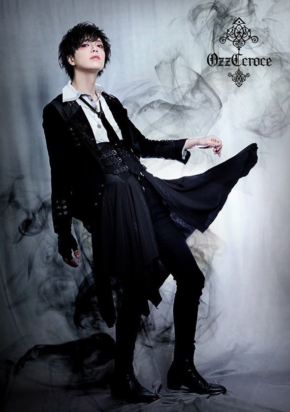 Model wearing an Ozz Croce outfit consisting of a white blouse, black jacket, and skirt pants, showcasing the brand's integration of fantasy motifs with a cool and edgy style.