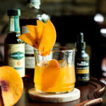 Peach Old Fashioned with peach slice and bourbon bottle