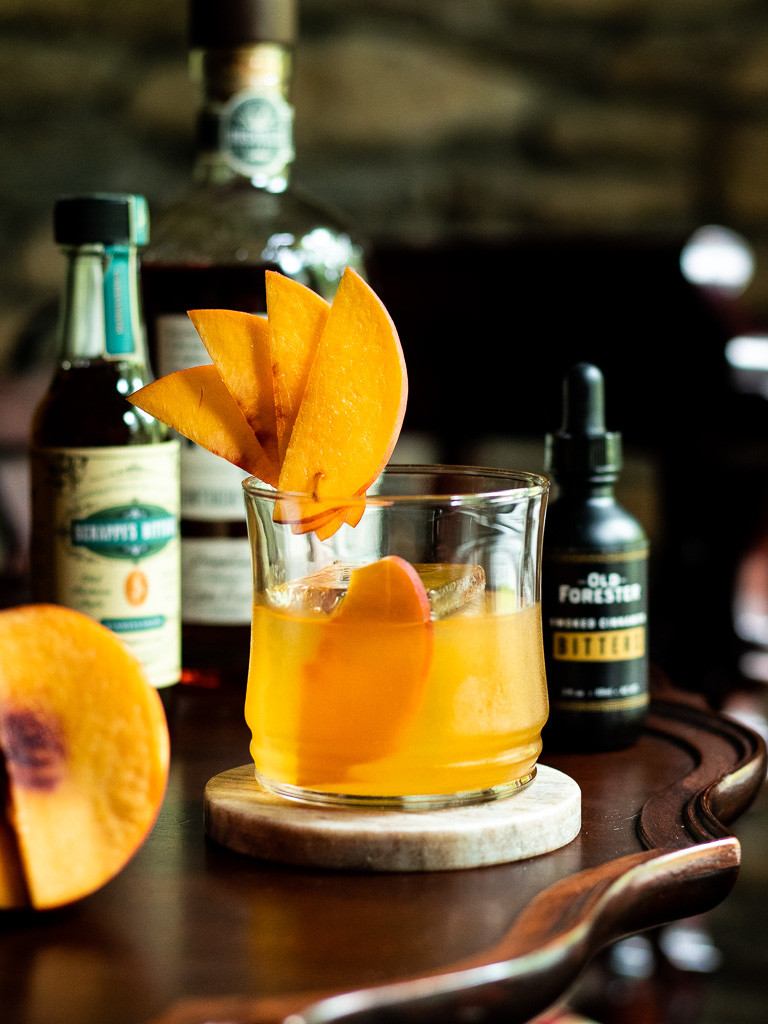 Peach Old Fashioned with peach slice and bourbon bottle