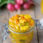 Close-up of homemade piccalilli in a glass jar, showcasing the mix of colorful chopped vegetables in a yellow mustard sauce