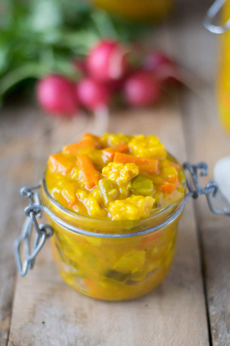 Close-up of homemade piccalilli in a glass jar, showcasing the mix of colorful chopped vegetables in a yellow mustard sauce