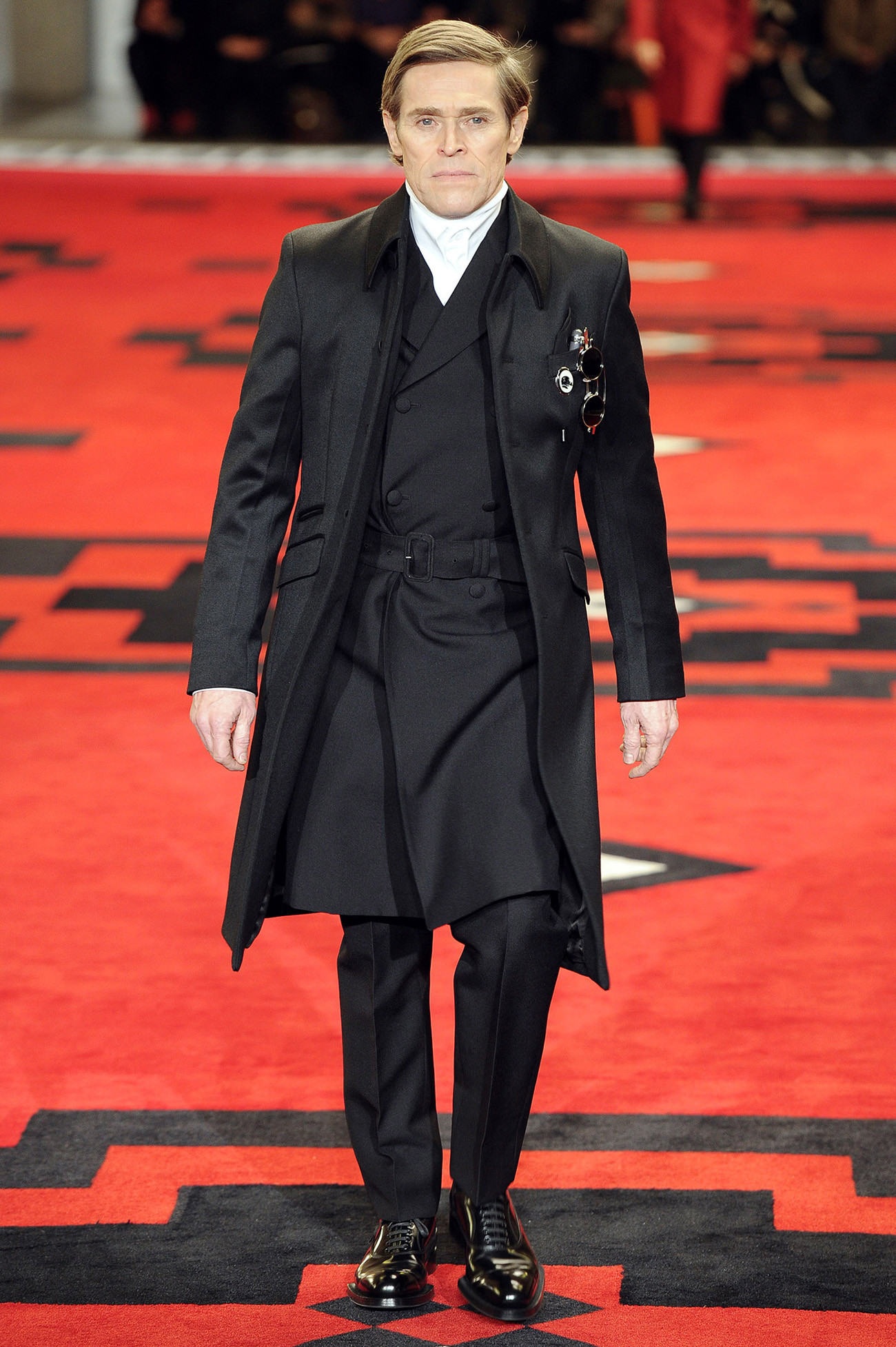 Willem Dafoe, renowned for his roles in "Spider-Man" and "Platoon," exhibiting Prada's Fall/Winter 2012 collection during Milan Menswear Fashion Week, personifying the show's villainous inspiration.