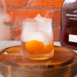 Smoked Old Fashioned cocktail on a wooden surface, smoke swirling around the glass
