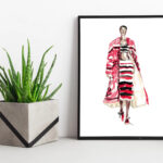 A framed fashion illustration print sits on a ledge next to a plant