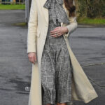 Kate Middleton wearing a black and white plaid dress and long white coat walking along a sidewalk