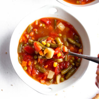 Homestyle vegetable soup in a white bowl with a spoon and bread