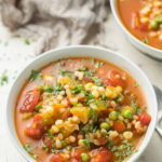 Two bowls of Vegetable Barley Soup on a white wooden surface with napkin; sustainable soup recipe.