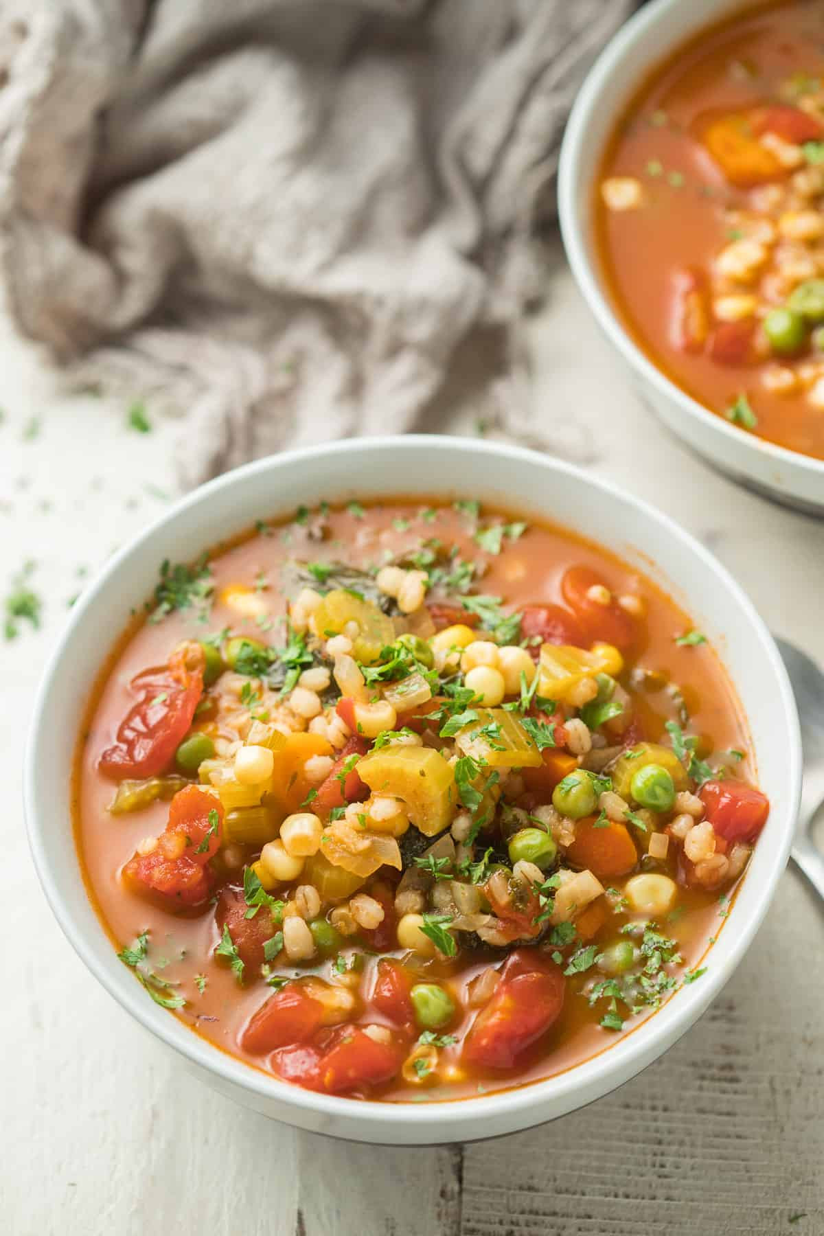 Two bowls of Vegetable Barley Soup on a white wooden surface with napkin; sustainable soup recipe.