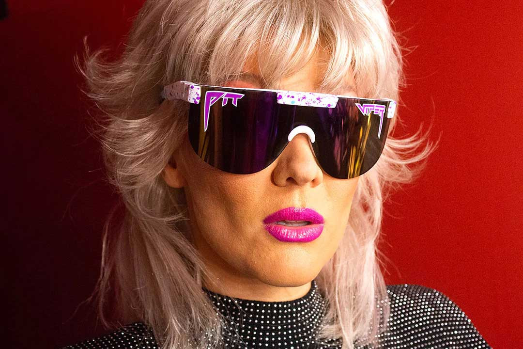 Woman with big hair and pink lipstick wearing mono-lens 80