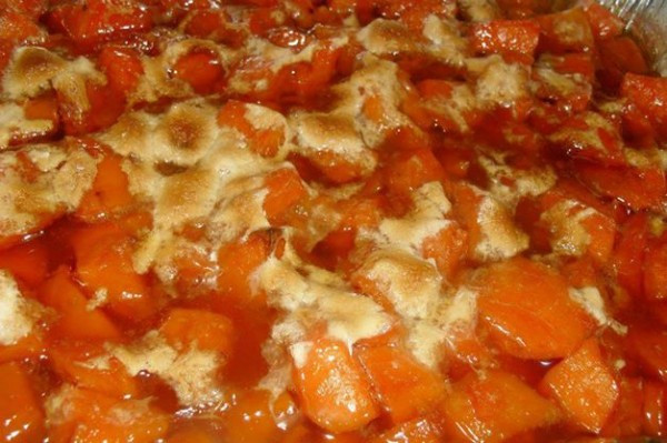 Close-up of candied yams with marshmallows, highlighting the sweet potatoes baked in a brown sugar syrup until tender and topped with mini marshmallows, showcasing the dish's texture and inviting appeal.