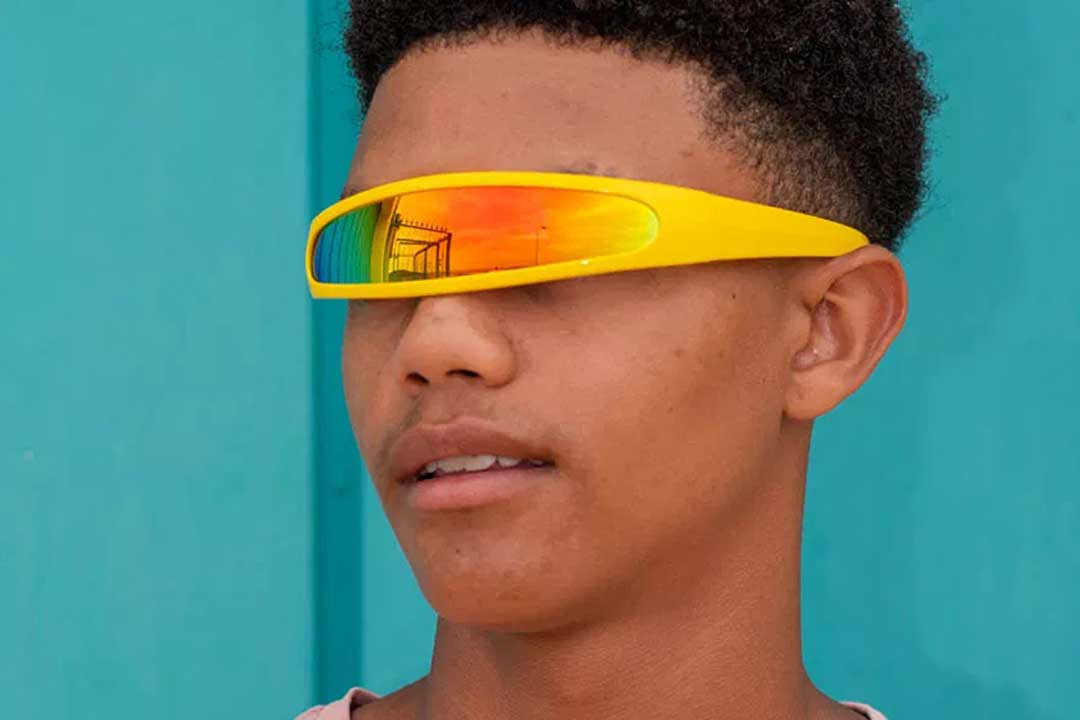 Young man wearing yellow robot sunglasses frame in front of blue background